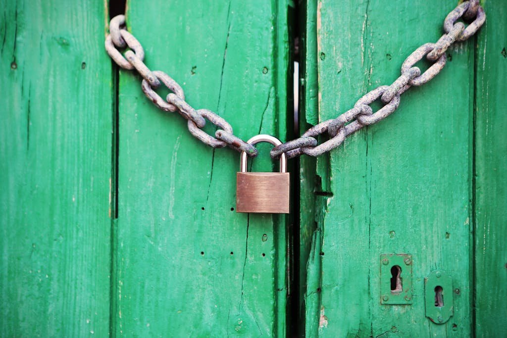 A rustic green wooden door secured with a heavy chain and padlock, symbolizing security. Une vieille porte verte sécurisée par une chaîne et un cadenas qui symbolise la liberté et les limites au droit de vendre un bien en viager du propriétaire.