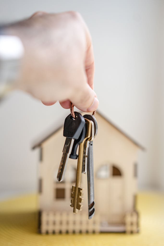 Focus sur une main qui tient trousseau de clés devant une maison. Cette image représente la cession ou l’acquisition d’un bien en viager.