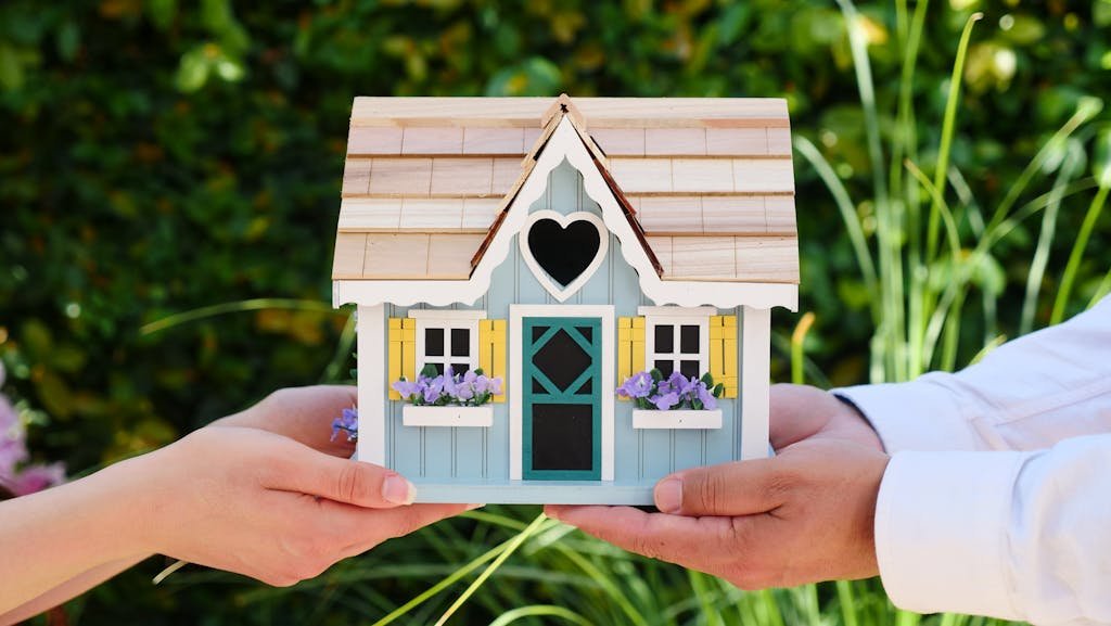 Gros plan sur des mains tenant une maquette détaillée de maison miniature, symbolisant les objectifs d’accession à la propriété, de cession d’un bien mais aussi dans notre cash de pouvoir continuer à vivre dans ce bien immobilier grâce au bail viager.