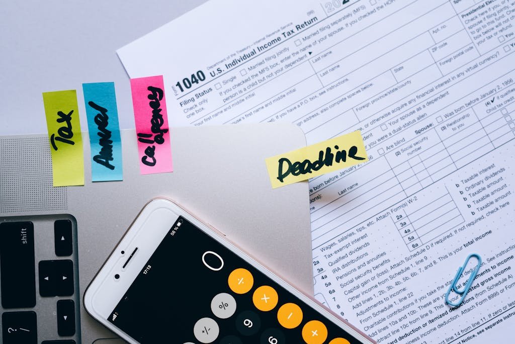 Bureau vu de dessus avec des documents fiscaux, l’application calculatrice ouverte sur un smartphone, des notes autocollantes et des trombones. Image qui représente le paiement de la fiscalité.